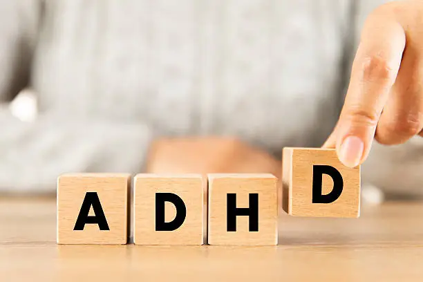 A hand placing a wooden letter D beside blocks spelling ADHD