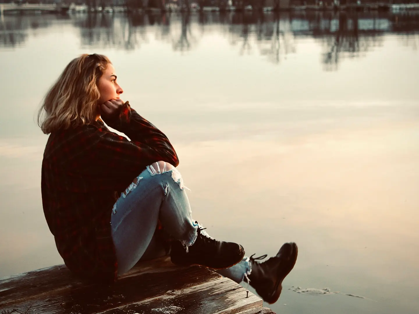 A woman sitting thoughtfully on a wooden dock beside a lake