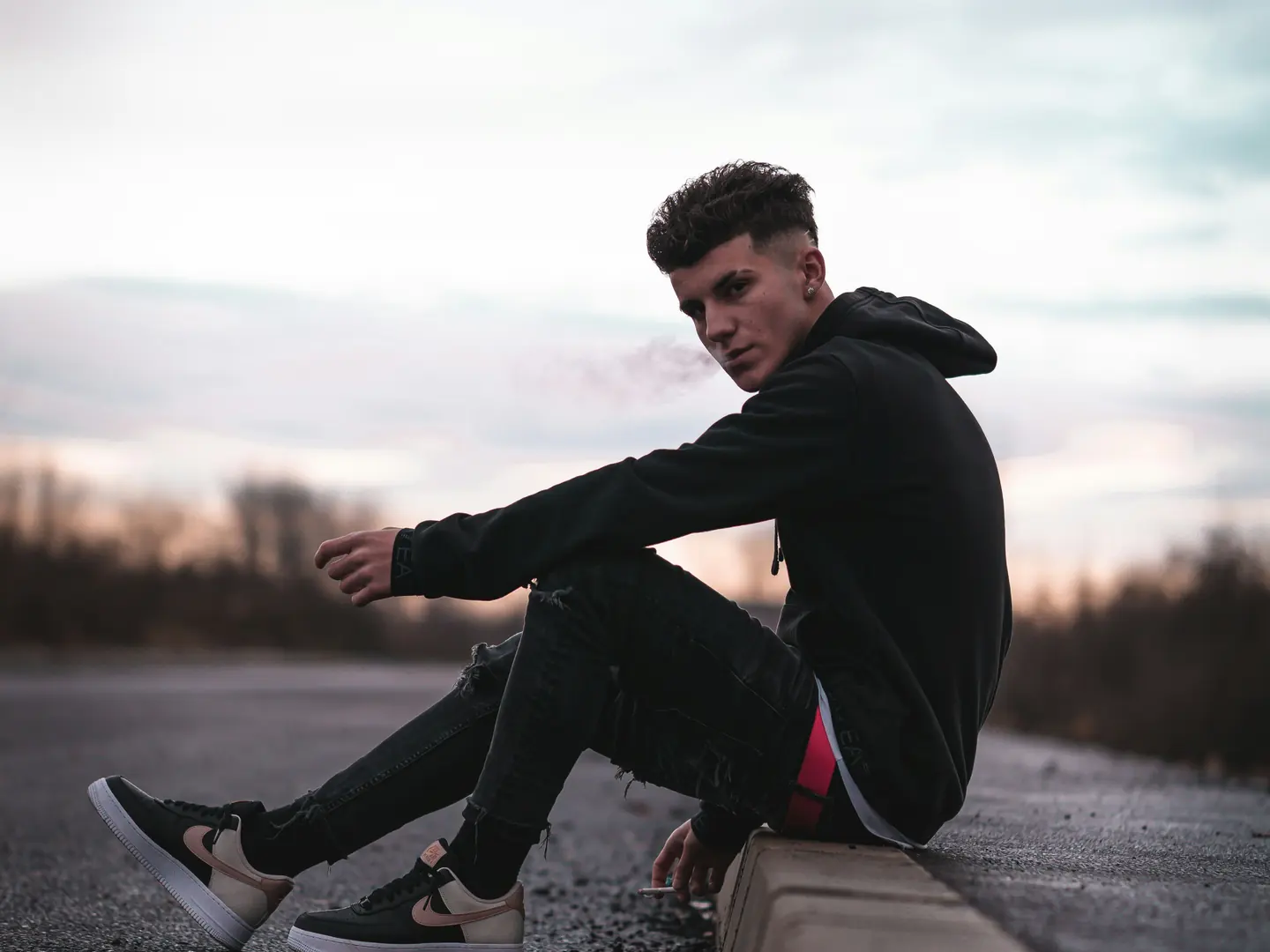 A young man in a dark hoodie sitting quietly outdoors